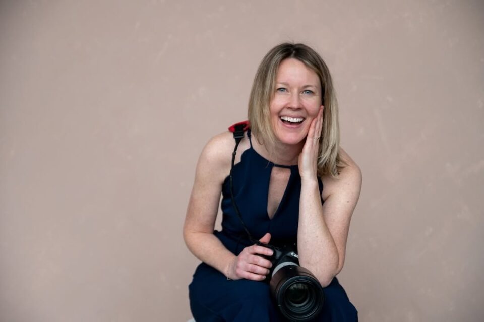 Calgary Wedding Photographer Shannon Hutchison holds her camera and smiles happily at the camera, wide view